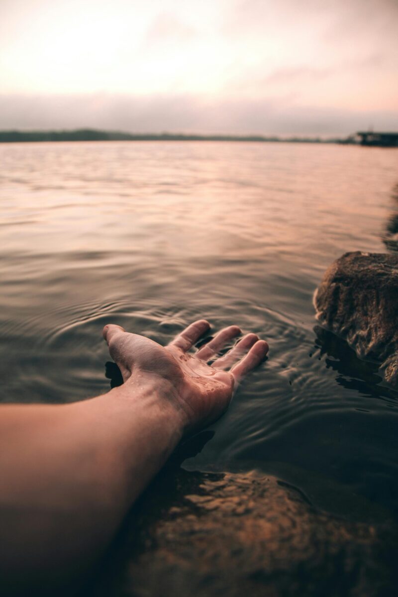 A serene image of a hand touching the water at twilight, creating gentle ripples.